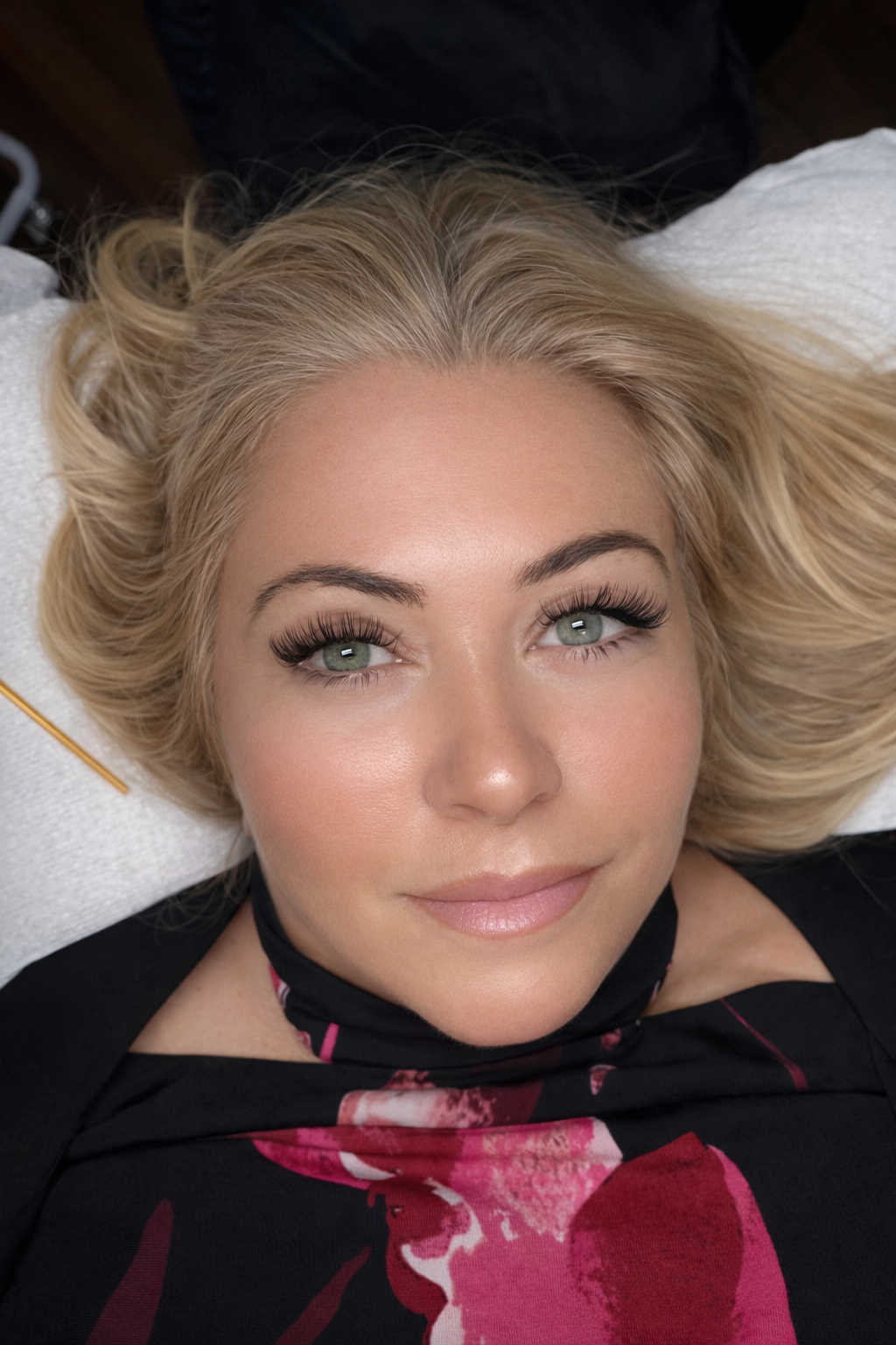 Close-up of a person with blonde hair and green eyes, wearing a floral top.