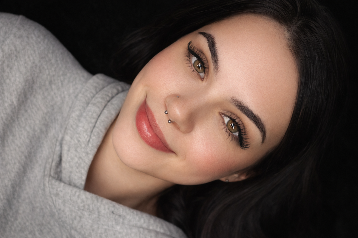 Woman with dark hair and gray sweater against a black background